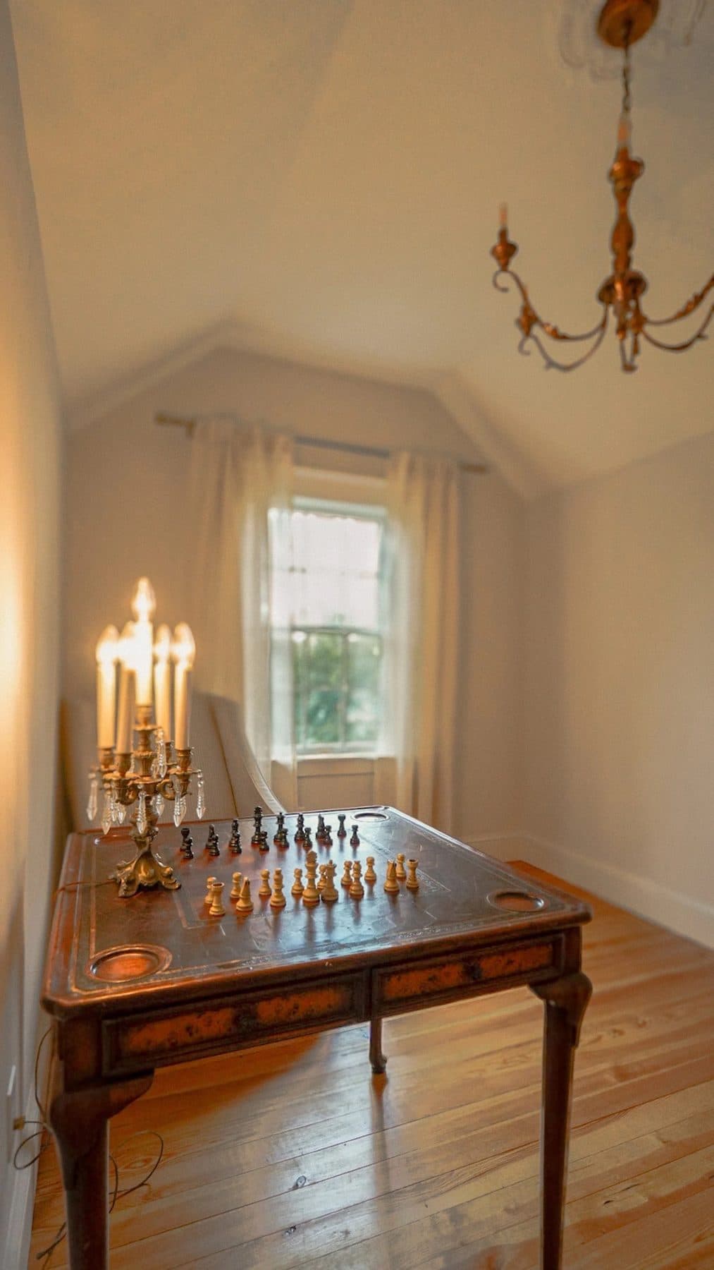 A candlelit antique chess table beneath a chandelier in the Thurston House game room
